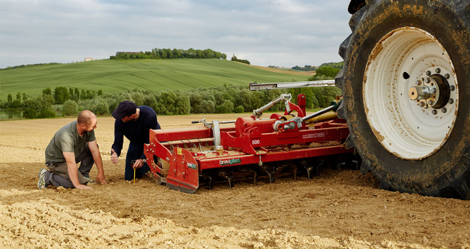 Un agriculteur accroupi tient de la terre dans ses mains